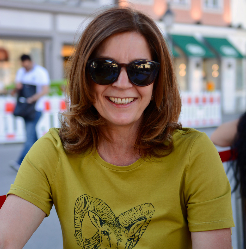 Frau mit moosgrünem Shirt, langen braunen Haaren und Sonnenbrille