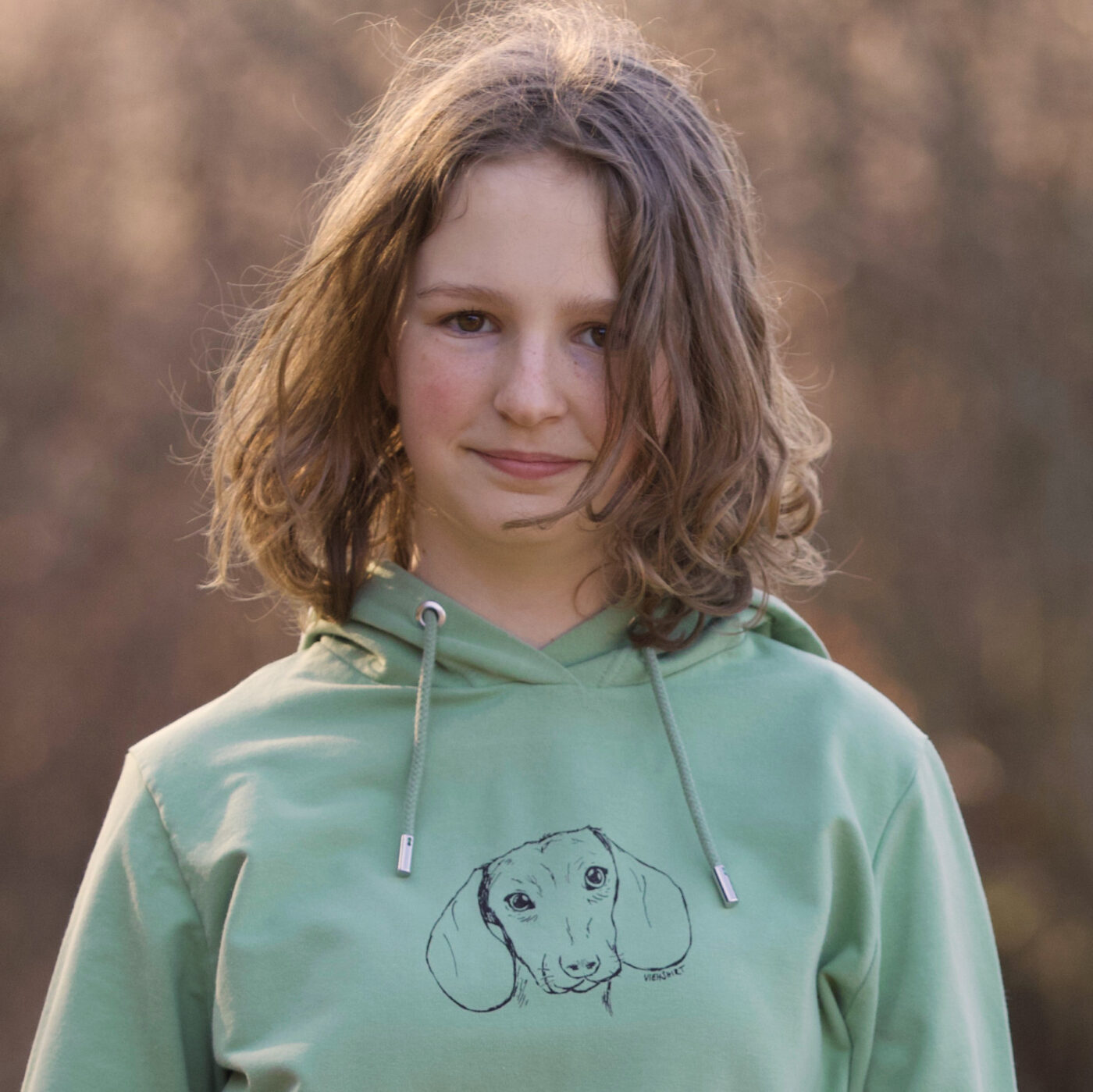 Junges Mädchen trägt grünen Hoodie mit Siebdruckmotiv Dackel