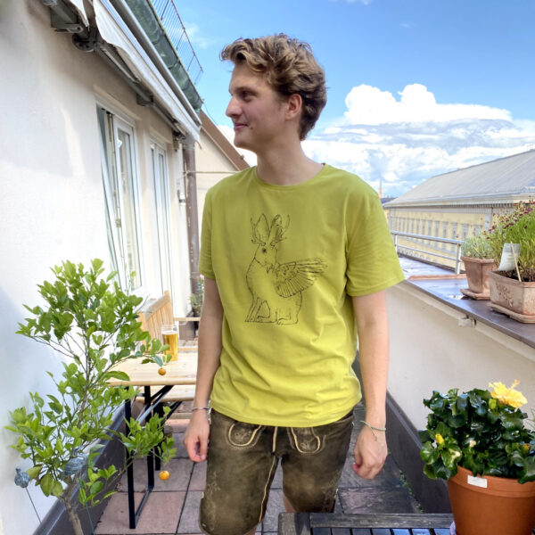Junger Mann trägt grünes Shirt mit Wolpertinger-Print auf Terrasse über den Dächern von München