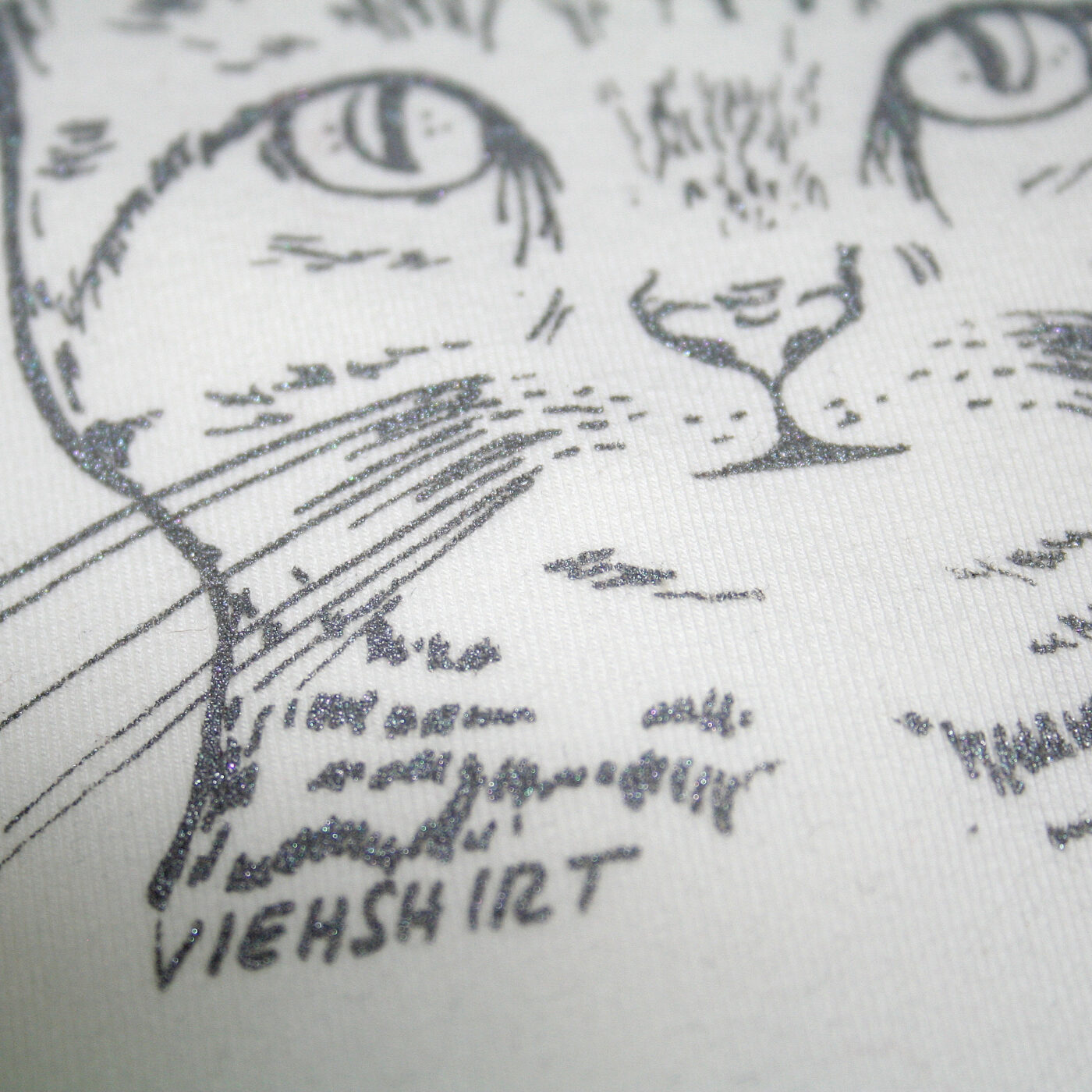Detail eines weißen T-Shirts mit silbernem Katzen-Kopf-Aufdruck