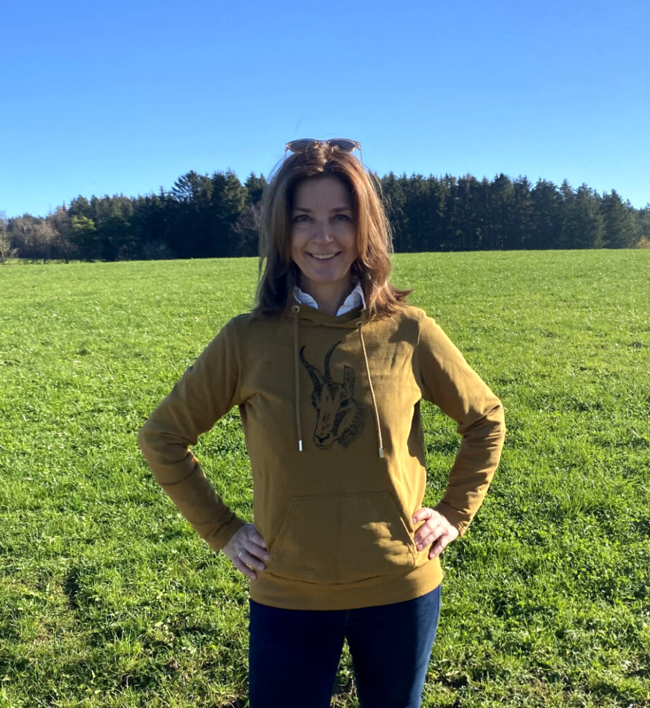 Frau vor grüner Wiese trägt braunen Hoodie mit Siebdruckmotiv Gamskopf