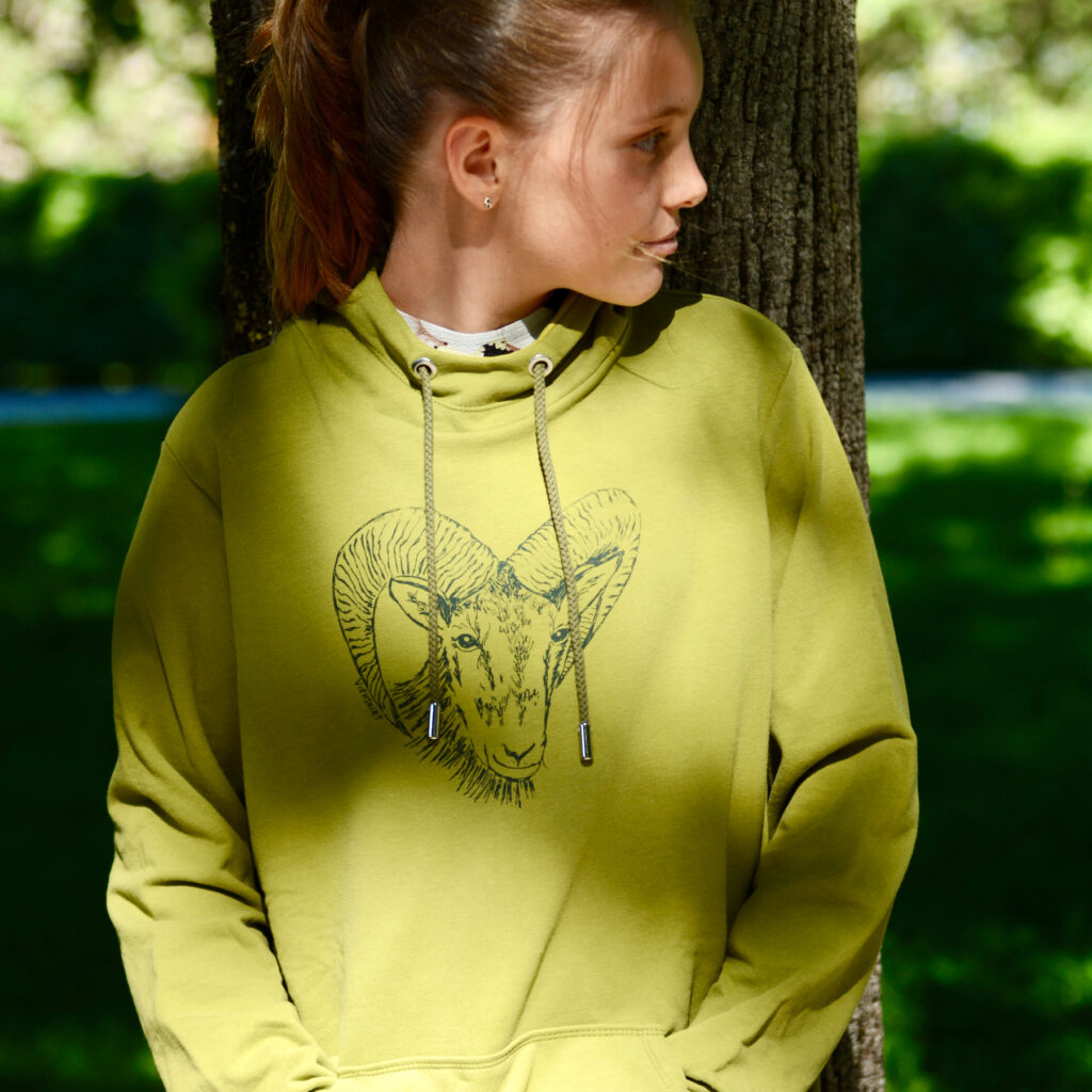 Frau an Baumstamm gelehnt. Sie trägt grünen Hoodie mit Siebdruckmotiv Mufflon