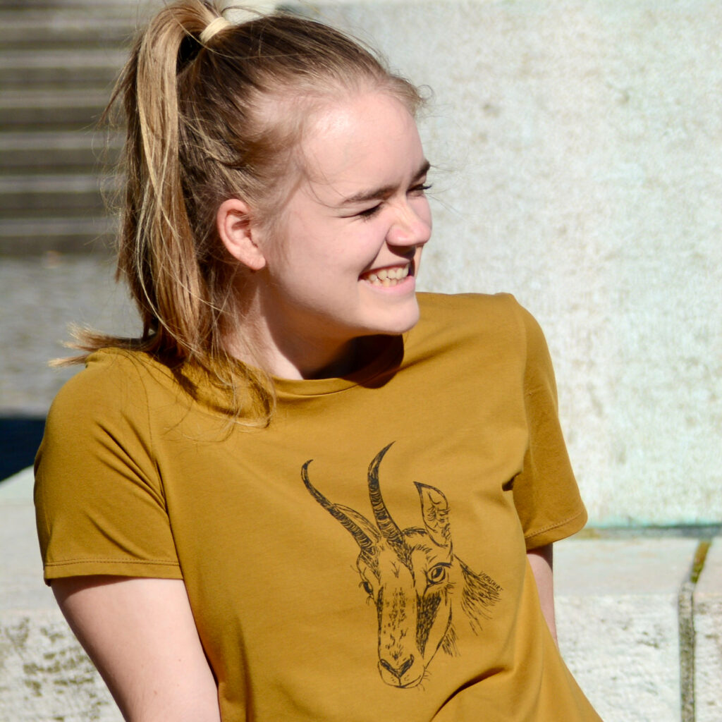 Frau vor Steintreppe, sie trägt ein ockerfarbenes T-Shirt mit Siebdruckmotiv Gamskopf.